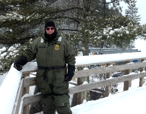 Photograph of person standing on snowy boardwalk and smiling with trees in the background