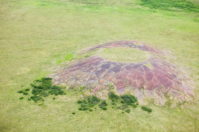 A conical earth formation rising from an otherwise flat tundra.