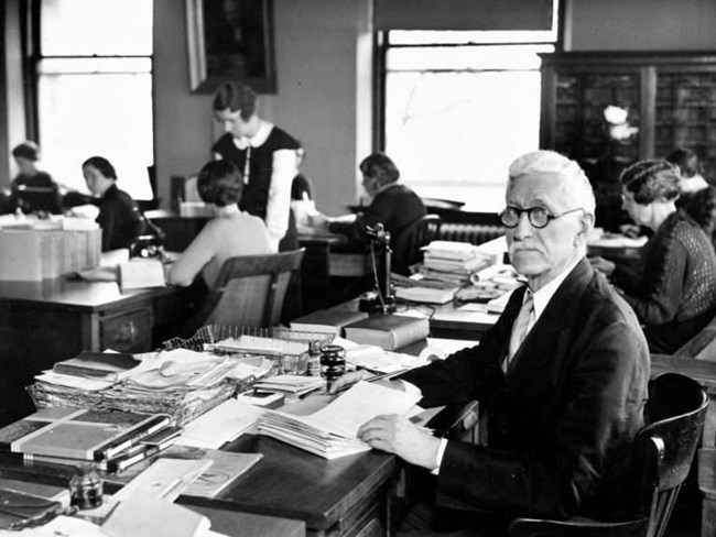 Portrait of Walter Plecker in an office at a desk covered in files