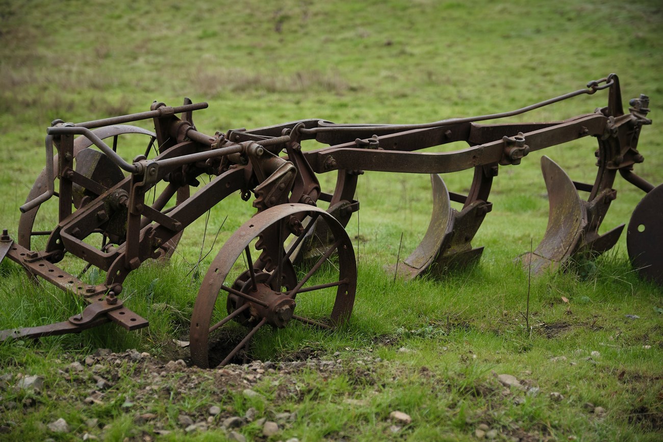 Dru Kelly Metal plow with three wheels and two grinders pushing into the ground.