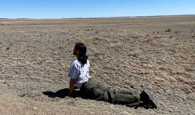 Park Ranger in cobra yoga pose, lying on grass while bending upward at waist and supporting upper part of body with extended arms and hands on ground.