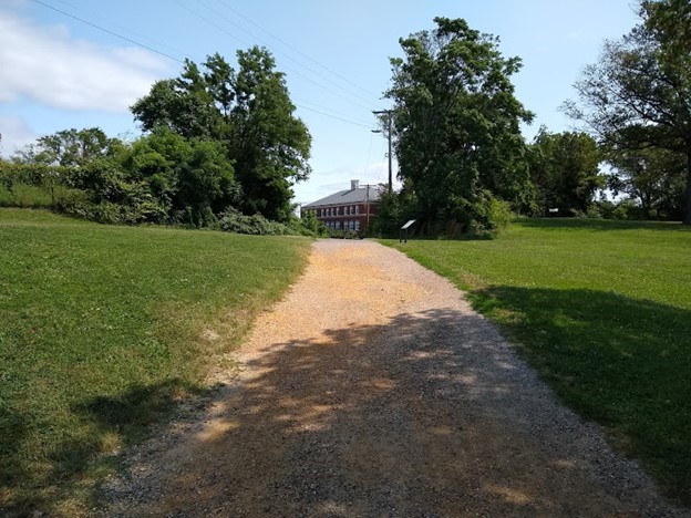 A dirt path cuts through green manicured grass towards a brick building