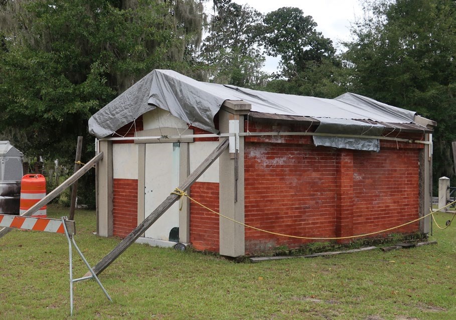 Temporary shoring placed around the walls of damaged brick mausoleum after a storm, the mausoleum also has a tarp over the roof.