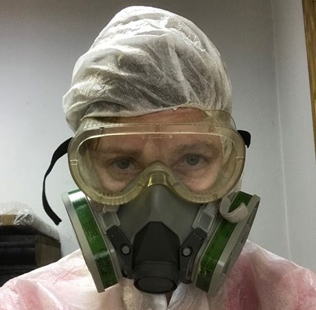 A woman with a respirator, protective goggles, and protective suit covering her clothes and hair