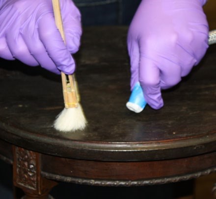 Worker using brush to dislodge mold from a wooden piece of furniture while simultaneously vacuuming the loose mold spore. Worker using brush to dislodge mold from a wooden piece of furniture while simultaneously vacuuming the loose mold spore.