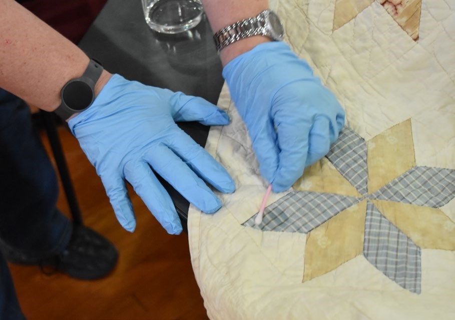 Preservationist demonstrating how to use a wet cotton swab to test the colorfastness of a heirloom quilt.