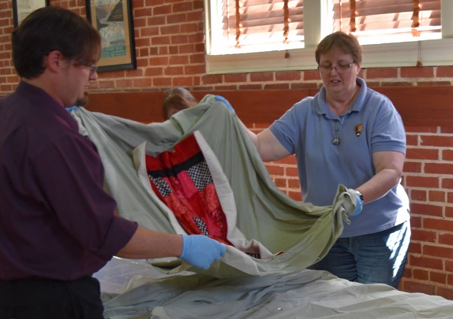 Preservationists demonstrating how to use a clean, dry sheet to support and lift a wet textile on to a work sufrace.