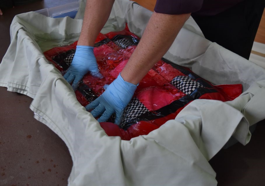 Preservationist demonstrating how to rinse a textile in a plastic bin of clean water. Preservationist demonstrating how to rinse a textile in a plastic bin of clean water.