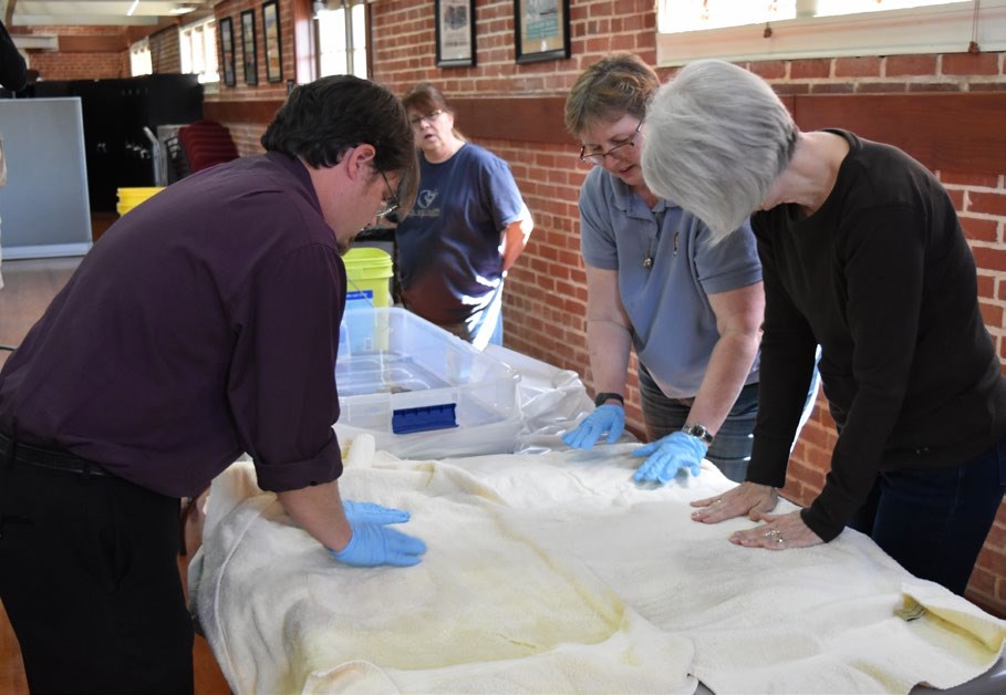 Preservationists blotting excess water from a flood-damaged textile using clean, dry towels