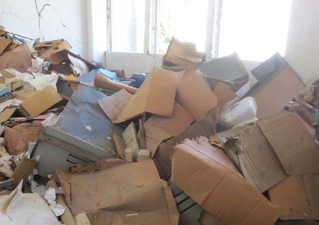 A photograph shows the devastation to a room housing books and documents after flood waters have receded. Cardboard boxes, books, and papers are in a large heap.