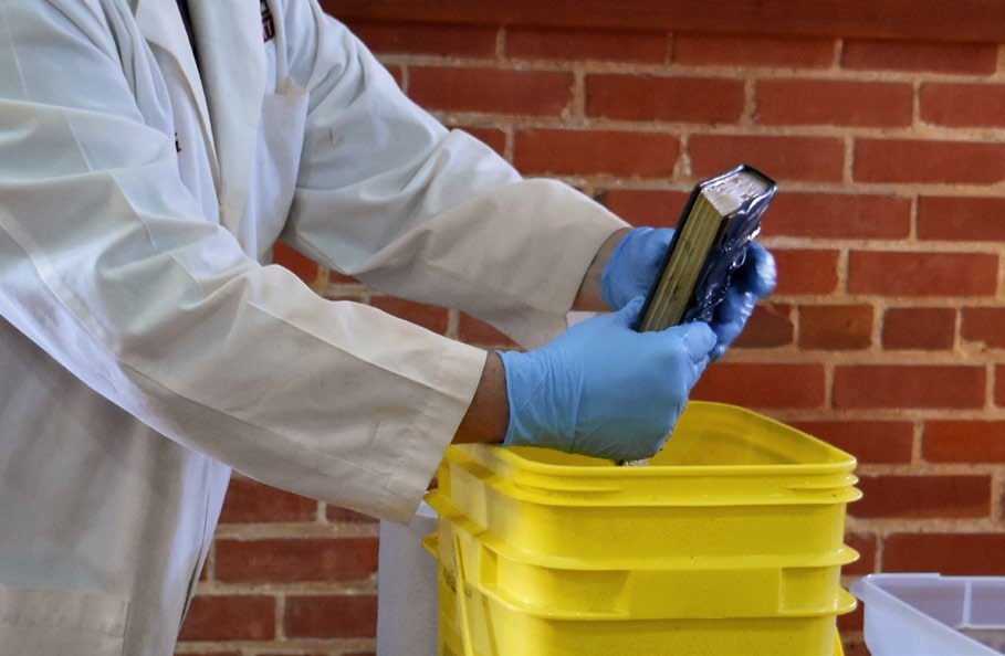 A photograph shows a preservation professional demonstrating how to tightly hold a book closed while rinsing it in a clean water bath. A photograph shows a preservation professional demonstrating how to tightly hold a book closed while rinsing it in a clean water bath.