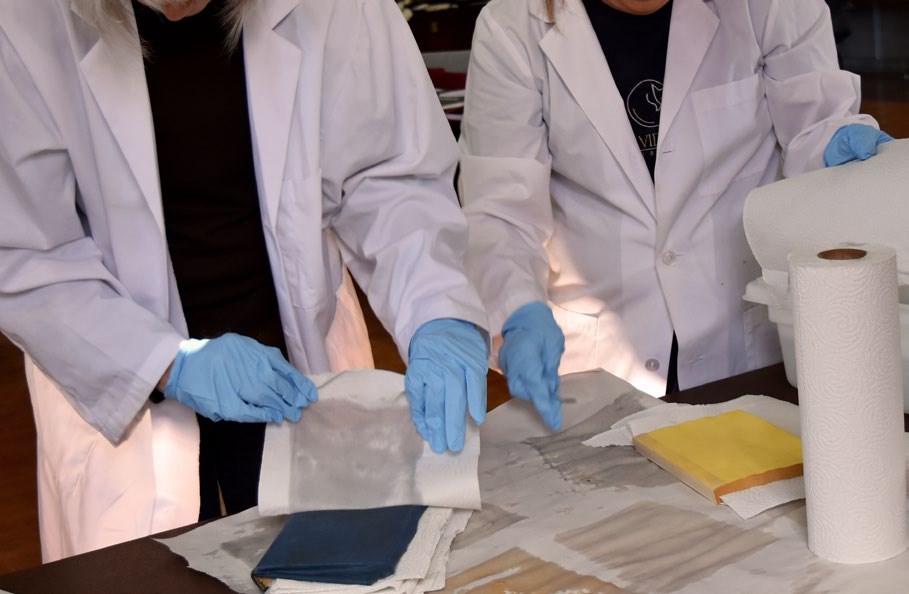 Two preservation professionals are shown placing paper towels between the pages of two wet books.
