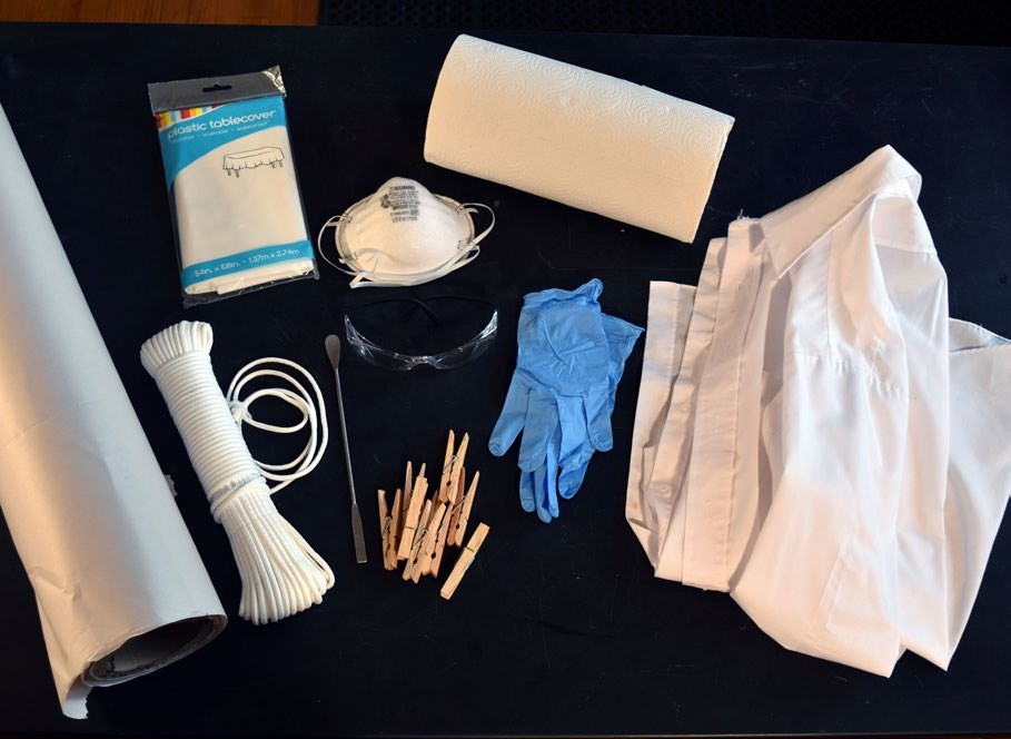A photograph shows standard supplies needed for recovering wet photographs including a smock, plastic gloves, N95 respirator, paper towels, clothespins, a plastic table cover, and a spatula. A photograph shows standard supplies needed for recovering wet photographs including a smock, plastic gloves, N95 respirator, paper towels, clothespins, a plastic table cover, and a spatula.