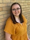 lt= Head shot of a young woman with brown hair in a yellow shirt.