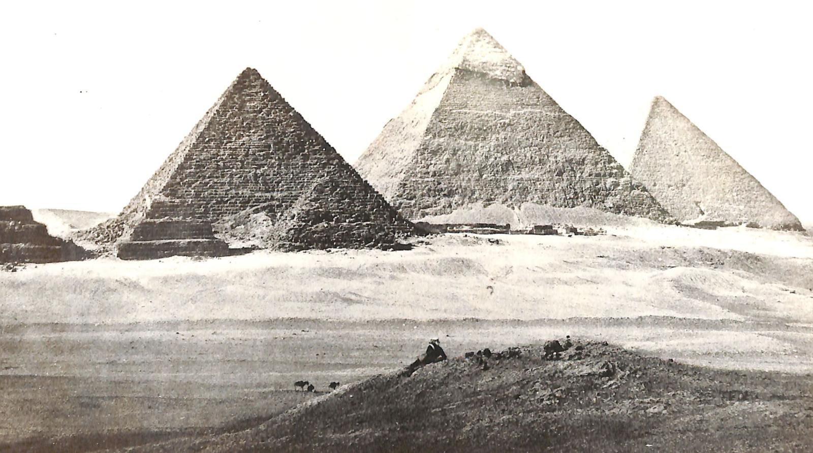 Black and white image with several pyramids of Giza in the background. A person lies on a hill overlooking the pyramids.