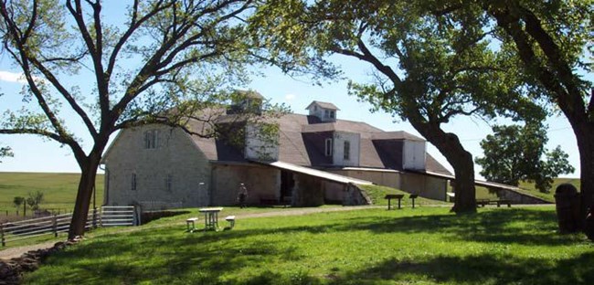 Limestone barn framed by cottonwood trees in foreground