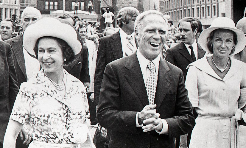 Queen Elizabeth II walking next to Boston Mayor Kevin White, followed by a group of people.