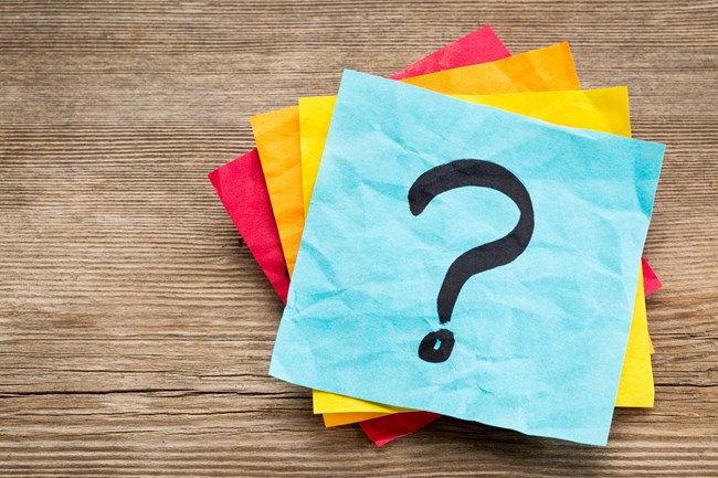 Stack of colored Post-It notes on a wood surface and a question mark drawn on the top