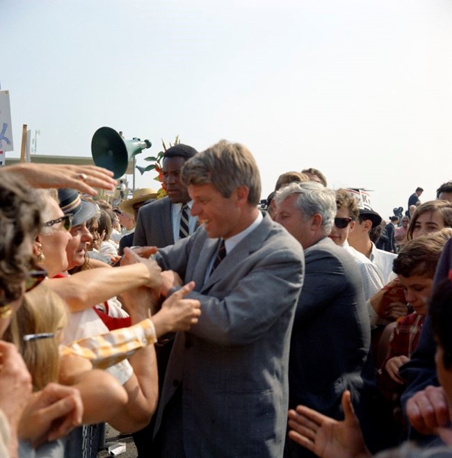 A color photo of RFK shaking hands in a crowd of people