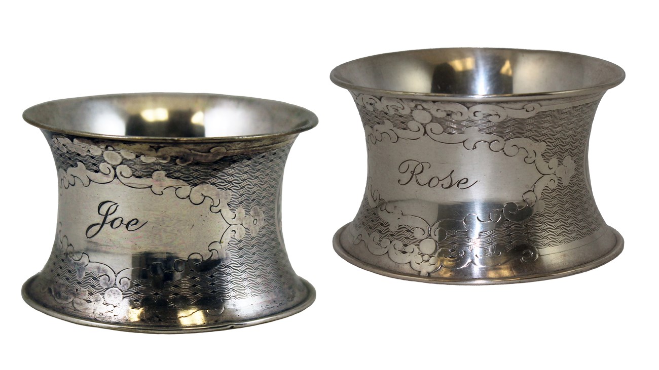 lt= Two silver napkin rings with floral decorations and names Rose and Joe engraved in medallions.