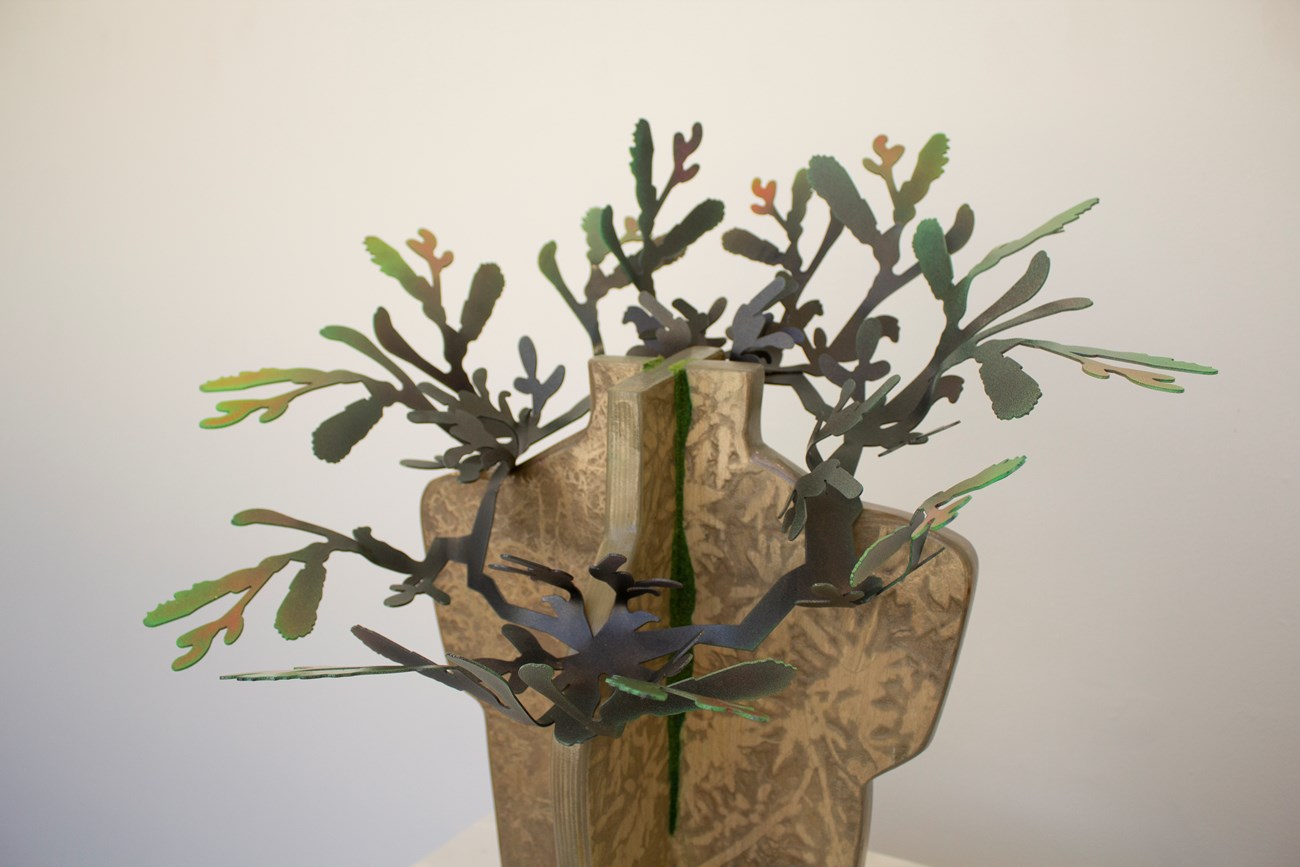 Metal artwork resembling leaves displayed on wood base