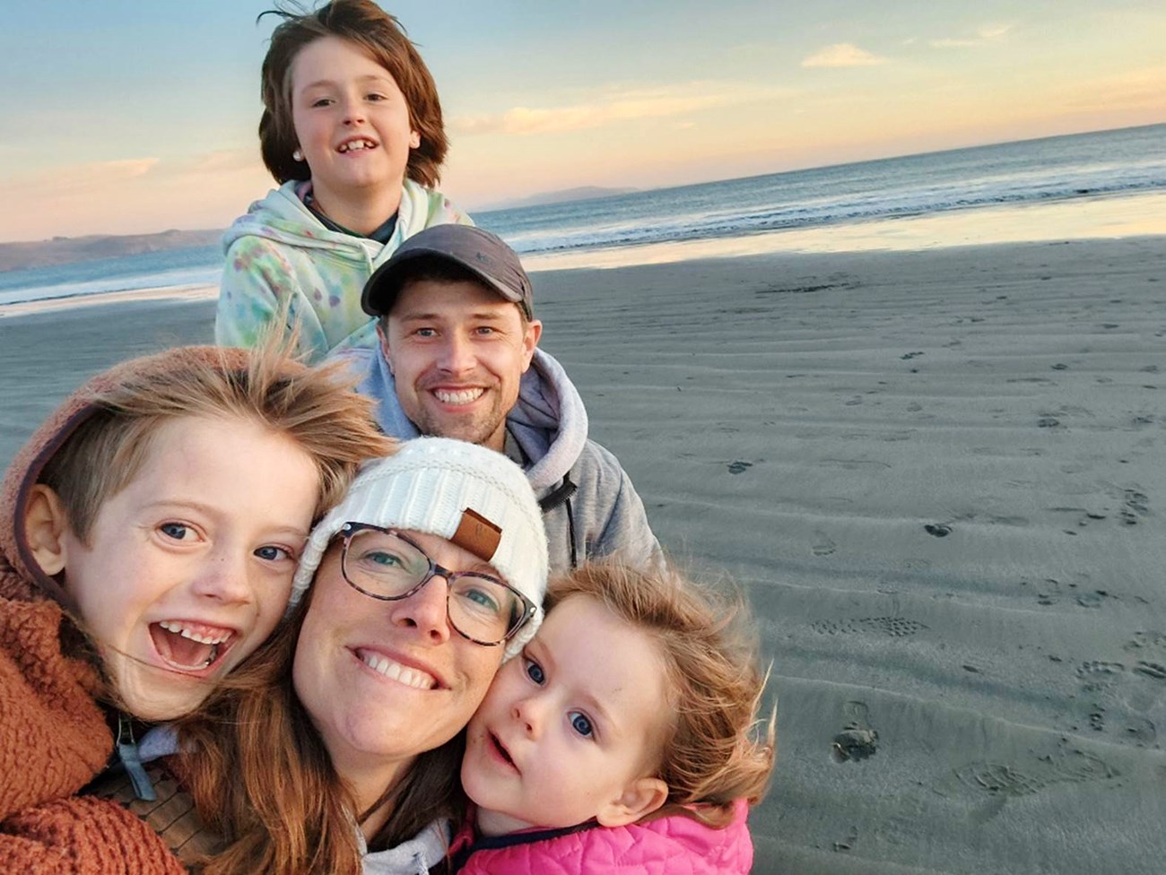 Rachel in a selfie with her husband and three children at the beach, all bundled in warm clothing.