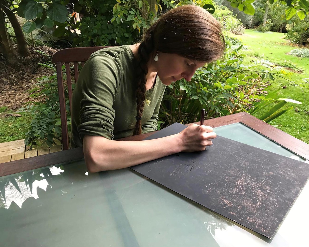 Woman leans over artwork in progress in an outdoor setting