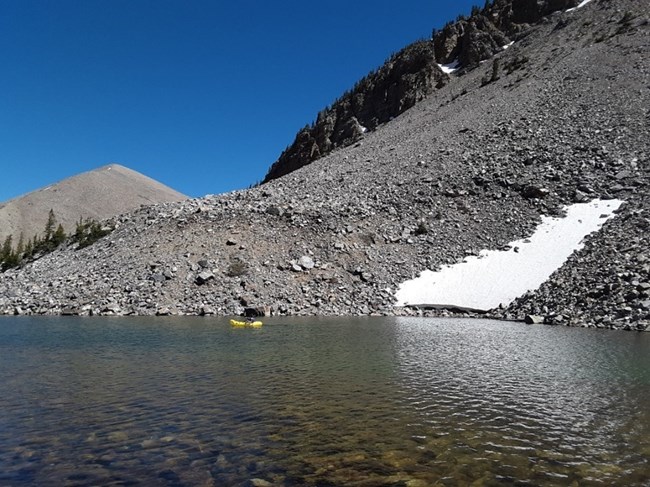 A yellow raft floating on Baker Lake with a talus slope in the background.