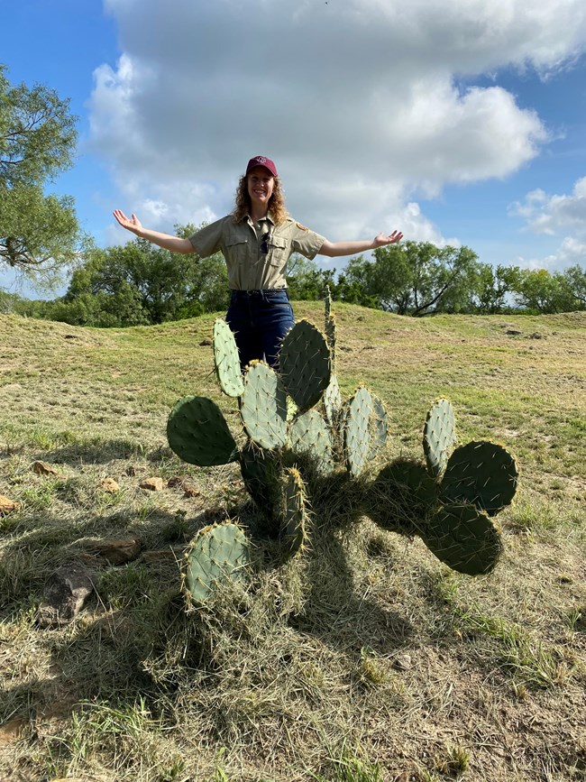 Woman stands in front of a prickly pear cactus with her arms wide open