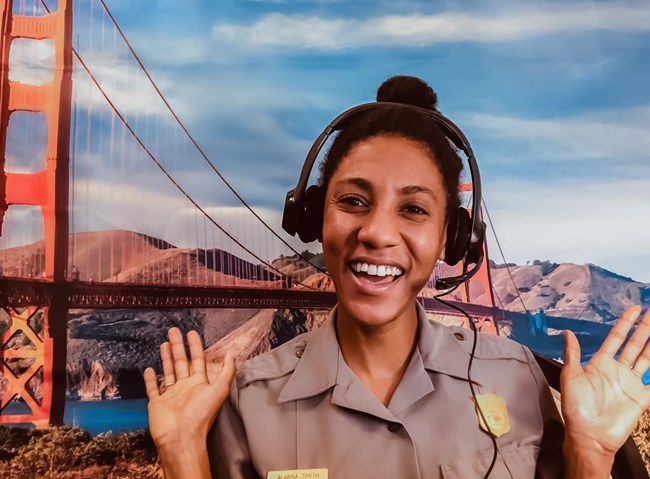 Ranger Alana teaching remotely Ranger Alana, a black woman, teaching remotely in front of a Golden Gate Bridge background.