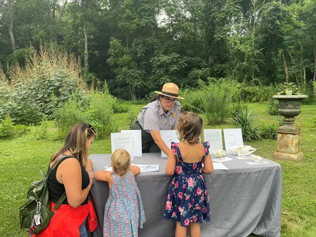 A ranger assisting children and their parent with an activity at a table.