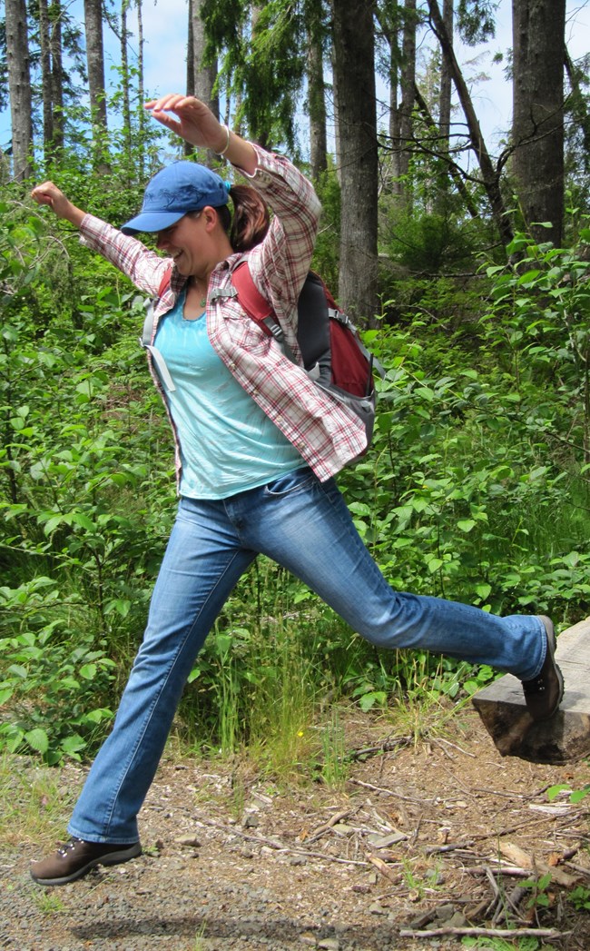 A woman leaps on a dirt trail while hiking.