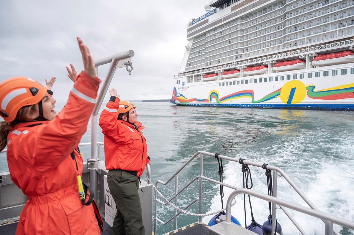 Ranger_cruise ship1_NPSSeanTevebaugh_web Two women in orange float coats and helmets wave to passengers on a passing cruise ship.