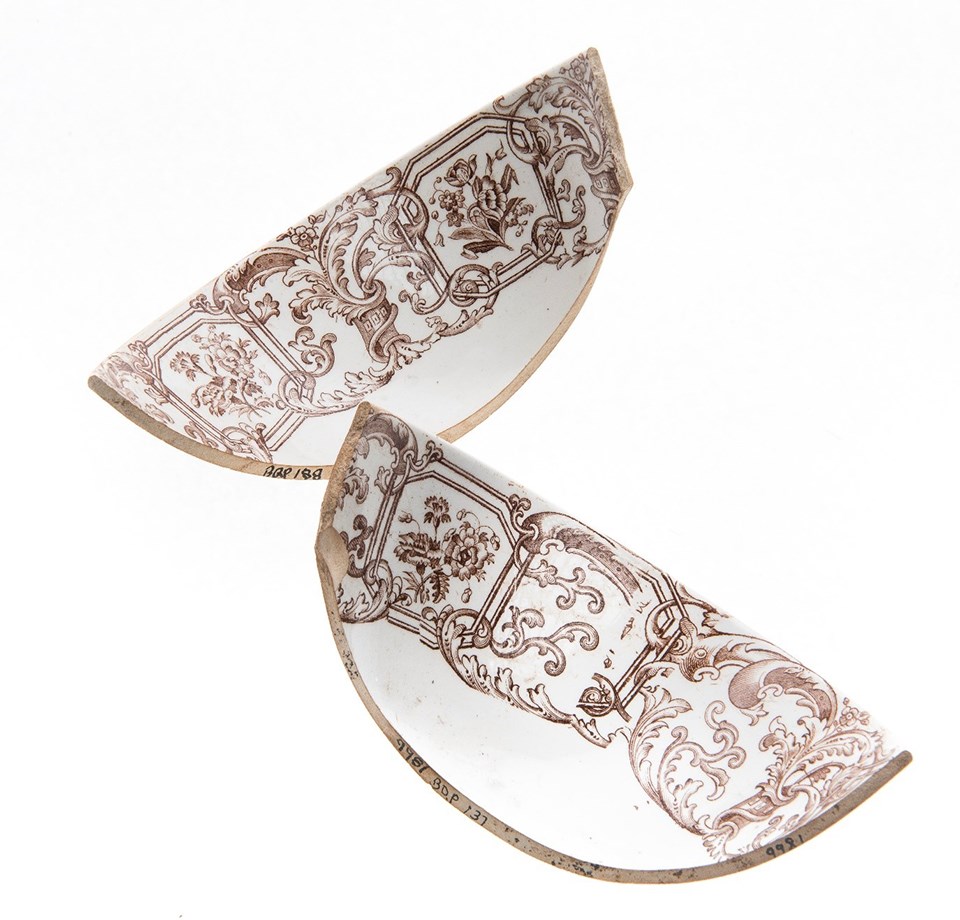 Two rim fragments from a white earthenware cup with a brown transfer printed pattern. The pattern includes flowers, acanthus leaves, and columns.