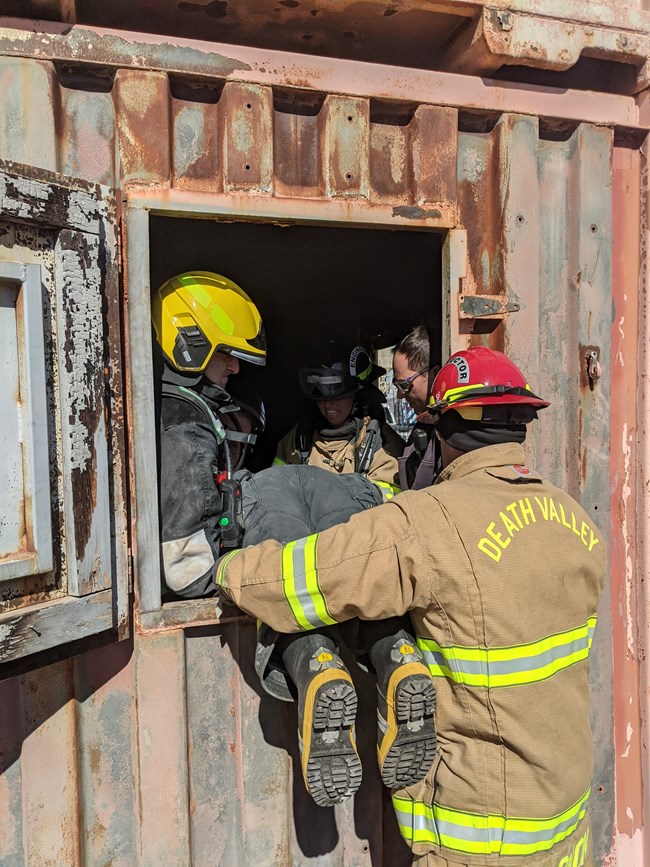 Rapid Intervention Crew Rescue Structural firefighters lower a person feet first through a window of a trailer.