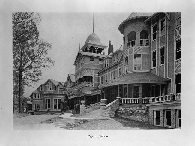 Multi-story Queen Anne-style building with asymmetrical facade and lots of windows. One rounded tower and one square tower masonry porch flank dominant front-facing gable.