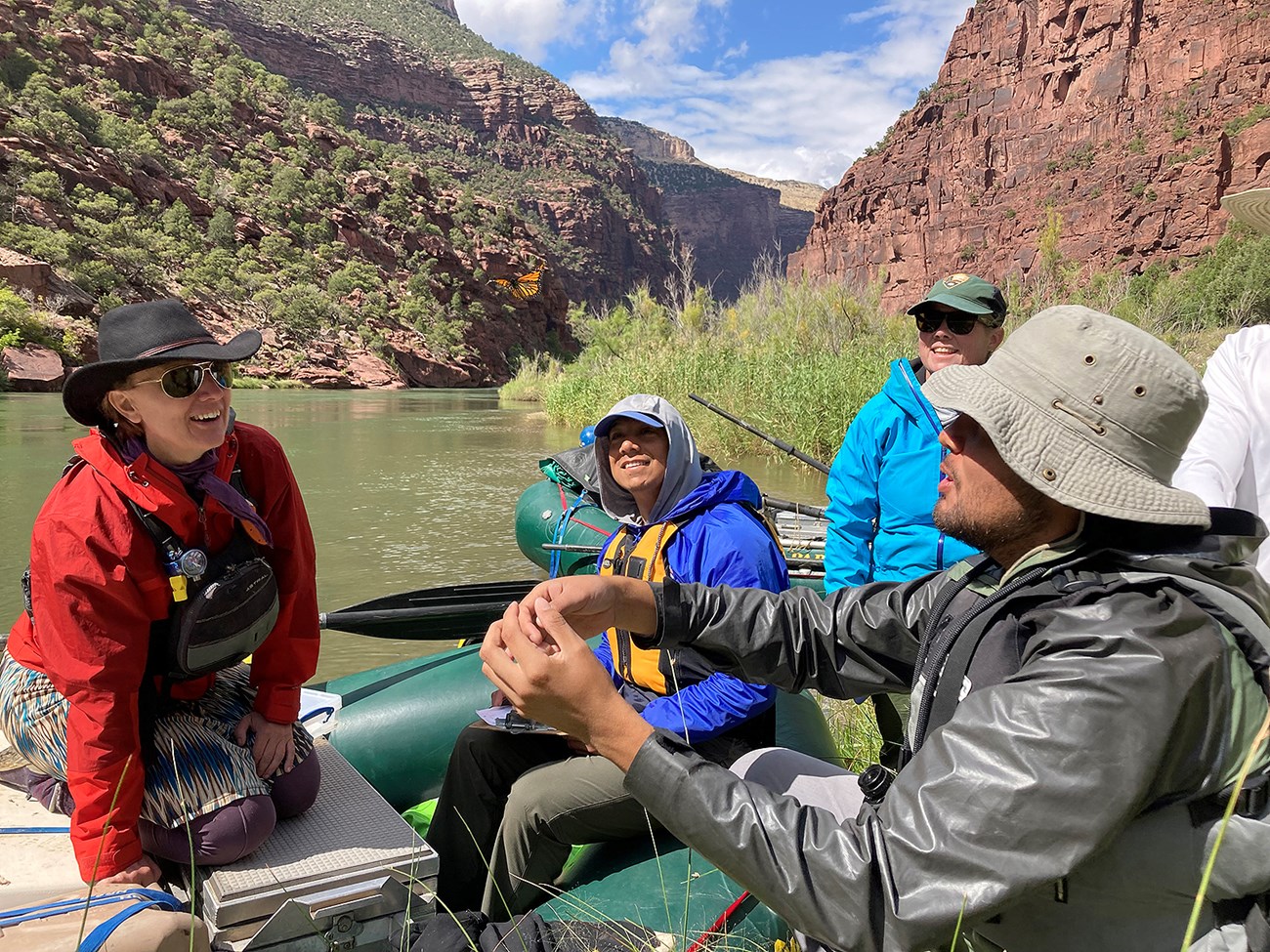 Releasing a monarch butterfly on the Green River A group of people in a raft watch a Monarch fly away from them. A river and high bluffs are in the background.