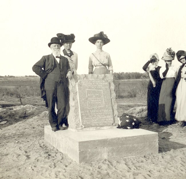 Black and white photo of a man standing with women at a stone marker