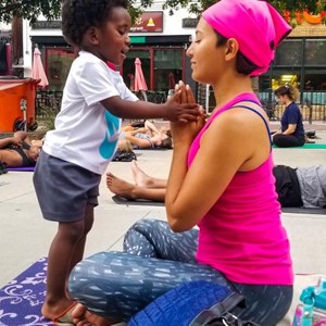 Riana Anderson, PhD, sitting cross-legged on a yoga mat while a small child holds her hands together in a pose