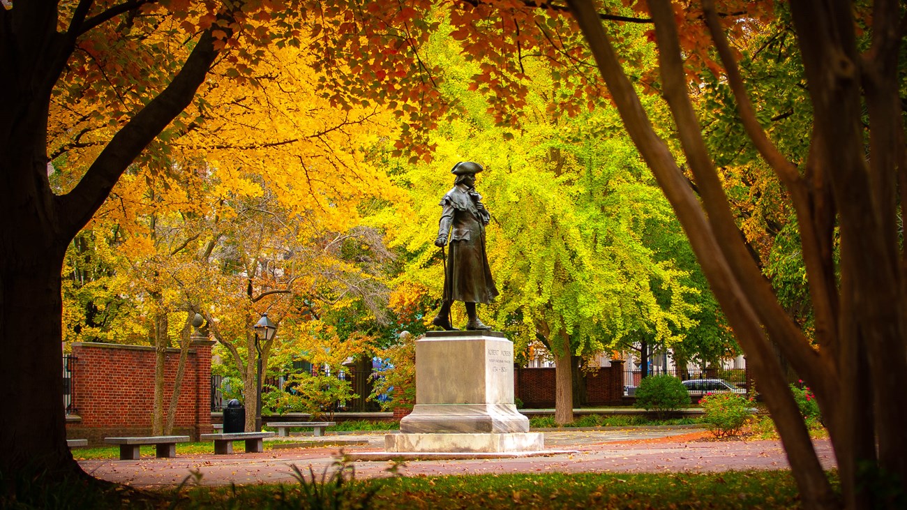 Statue of a man on a pedestal surrounded by deciduous trees