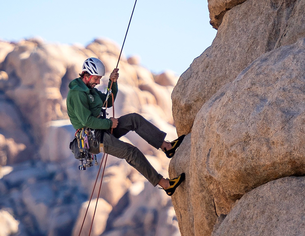 Man with helmet hangs from ropes off a rocky cliff