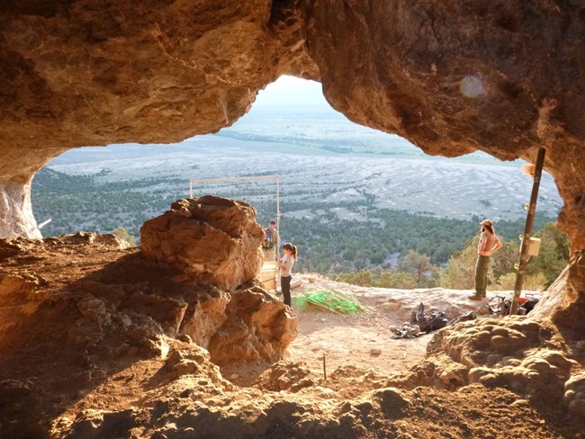 Picture from inside the mouth of a cave facing out with staff and volunteers setting up nets in the mouth to catch bats as they leave the cave entrance.