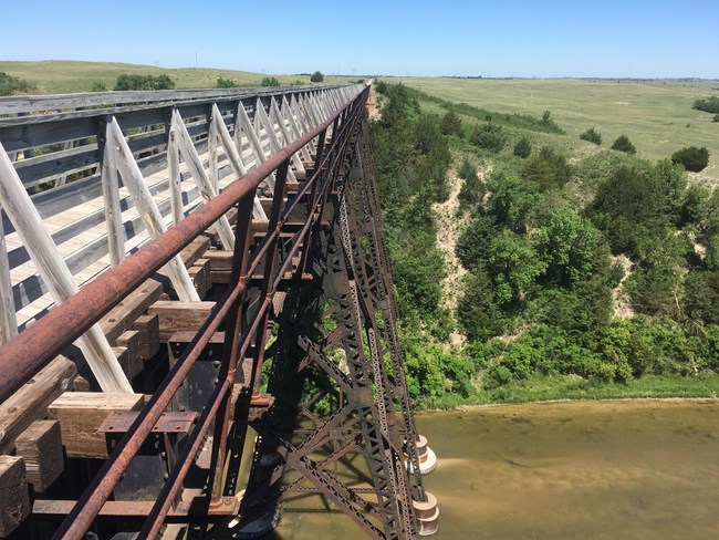 To the right the Cowboy Trail Bridge crosses the Niobrara River, looking down you can see the bridges tussles. Looking into the distance you can see the end of the bridge and prairie.