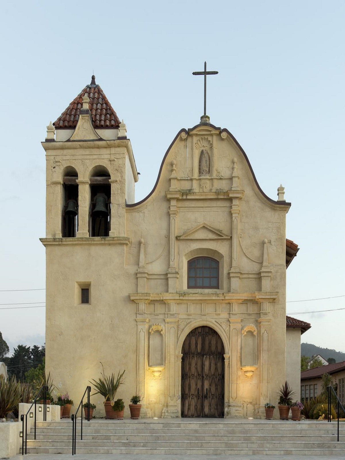 Tan building with a rounded roof, tall door, and square bell tower attached to the left