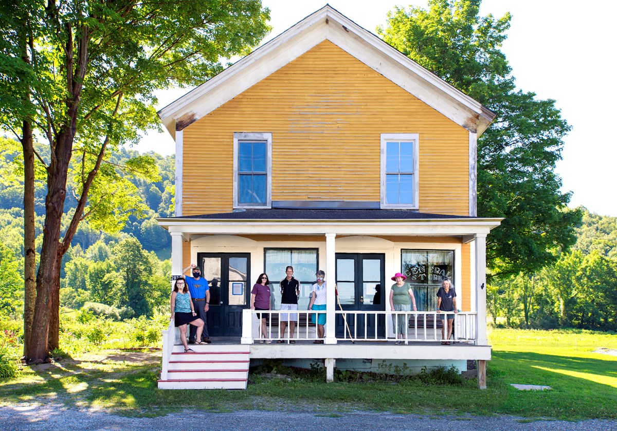 Sheldon Store in Rupert, Vermont. A  two story wooden gabled structure with painted yellow clapboards and two sash windows on the second story. The first story has a white wooden porch with people standing for the photo.