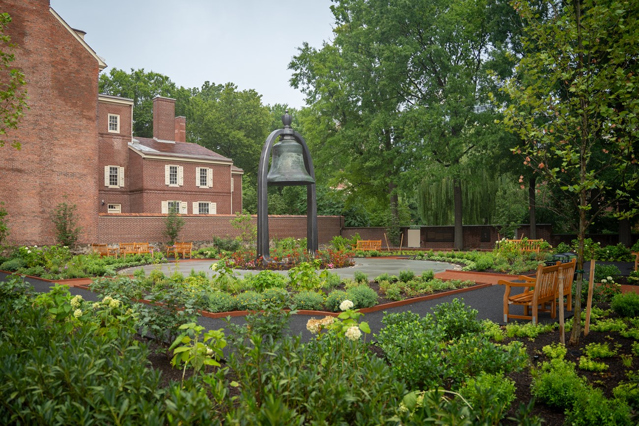 Benjamin Rush Garden Tree and flowers surrounding gravel paths and a large bell in the middle.