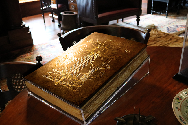 Brown historic book with gold imagery on the cover displayed on a table.