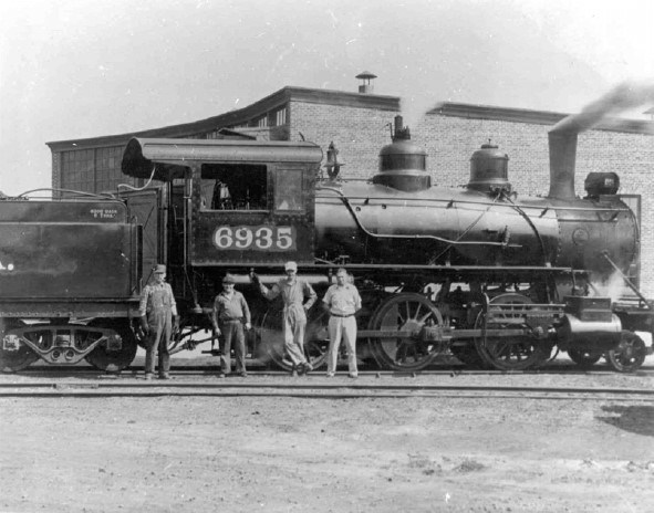 four men in work attire stand in front of a train