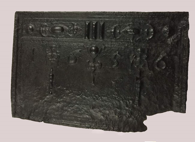 Black cast iron fireback with raised decorations dated 1656.