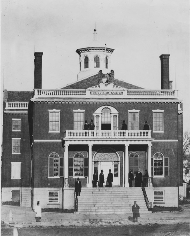 Historical black and white photo of men standing in front of two-story brick building.